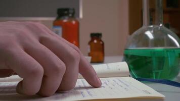 A researcher in a lab writes notes and consults a book, exploring video