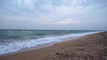 Experience a serene sandy beach with waves crashing on a cloudy day video