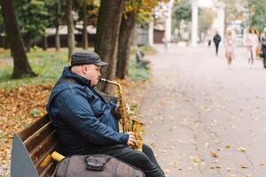 A saxophonist performs in a serene park during autumn while seated on a bench photo