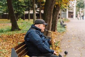 A saxophonist performs in a serene park during autumn while seated on a bench photo
