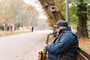 A saxophonist performs in a serene park during autumn while seated on a bench photo