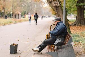 A saxophonist performs in a serene park during autumn while seated on a bench photo