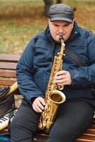 A saxophonist performs in a serene park during autumn while seated on a bench photo