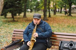 A saxophonist performs in a serene park during autumn while seated on a bench photo