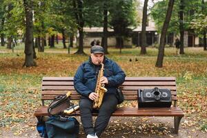 A saxophonist performs in a serene park during autumn while seated on a bench photo