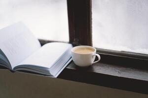 Cozy winter day with steaming coffee, open book, and candlelight by the snowy window photo