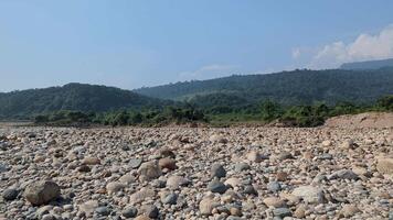 Exploring the rocky riverbed in a secluded valley during a clear day amidst lush green mountains video