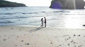 Man and Woman Walking Along Tropical Beach at Sunset, Tracking aerial shot of young couple on vacation having fun on the beach. Couple walking on empty beach at sunset by the beach. video