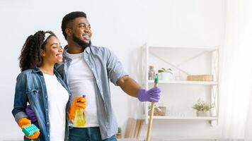 Happy Black Couple Standing In Fresh-Cleaned Living Room And Looking Aside, Satisfied After Successful Tidying, Copy Space photo
