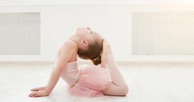 Little ballerina in split on floor, copy space. Smiling baby girl dreaming to become professional ballet dancer, classical dance school photo