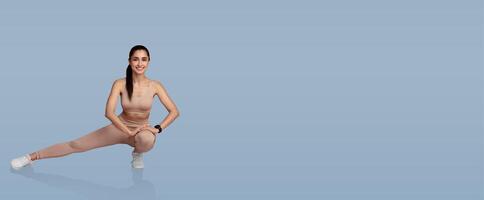 A young woman performs a side lunge, showcasing flexibility and balance. She exudes confidence while dressed in matching workout attire against a soft blue backdrop. photo