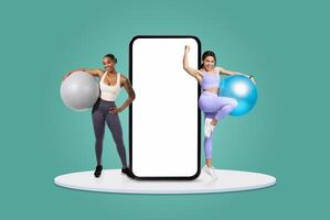 Two women engage in a workout routine using fitness balls. One holds a gray ball while the other poses with a blue one. They stand prominently in front of a large blank mobile device. photo
