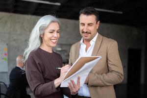 A woman and a man engage in a collaborative discussion in a modern office. The woman writes on a notepad while the man listens attentively, both smiling as they share insights. photo