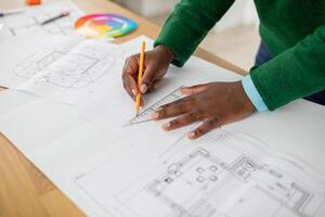 A person is focused on designing architectural plans using a ruler and pencil on a wooden table. Color samples are visible, indicating attention to design details, in a clean workspace. photo