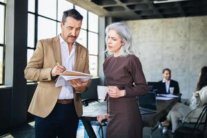 Two colleagues engage in a focused discussion while reviewing notes in a contemporary office. Others work in the background, contributing to a collaborative atmosphere. photo