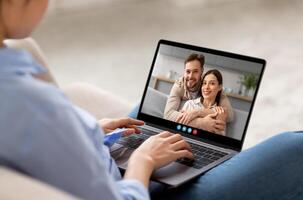 A woman sits comfortably on a couch, connecting with a friendly couple through a call on her laptop, showcasing a warm and engaging conversation in a cozy setting. photo