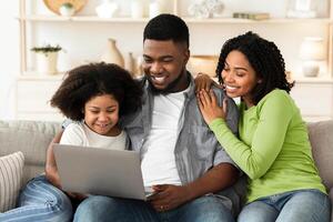 Loving African American Family Of Three Resting On Couch With Laptop, Spending Quarantine Time At Home Together, Surfing Internet Or Watching Movies photo