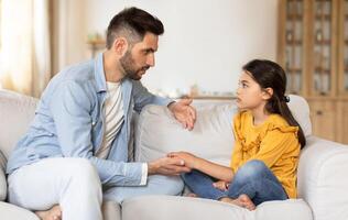 Supportive Arabic Dad Talking To Sad Preteen Daughter, Supporting Her In Childhood Struggles, Sitting On Couch, Explaining Something And Helping Cope With Adolescence Problems At Home photo