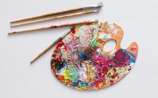Art palette with colorful paint strokes and paintbrushes on white isolated background, top view, flat lay, object photo