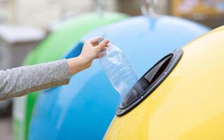 Waste Recycling Concept. Unrecognizable lady throwing plastic bottle into yellow recycle bin container outdoors, sorting garbage, enjoying zero waste living, cropped image with selective focus photo