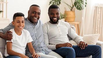 Africam American Grandfather With Son And Grandson Relaxing Together At Home, Embracing On Sofa, Looking At Camera And Smiling photo