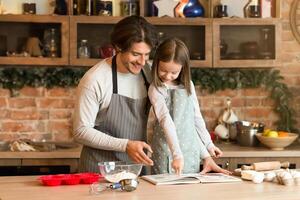 Dad and little daughter in kitchen cooking pastry together, checking recipe in coolinary book, copy space photo