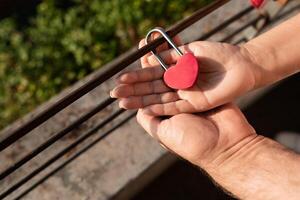 A couple shares a romantic moment as they place a heart-shaped padlock on a railing, symbolizing their love. This heartfelt gesture captures their connection in a serene outdoor setting. photo