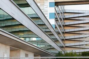 A contemporary building features sleek glass panels reflecting its geometric design. The architecture showcases innovative lines and textures against a clear urban backdrop. photo