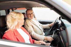 A man and a woman are engaged in a light-hearted conversation while sitting inside a car. The atmosphere is relaxed, with sunlight illuminating the interior. photo