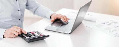 Payroll Concept. Close up of middle-aged accountant using calculator and computer, selective focus photo