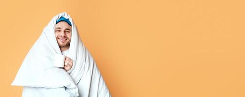 Smiling guy in blanket is holding cup on yellow background, free space photo