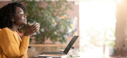 Side view of delighted black girl freelancer enjoying coffee at cafe, having break while working online, empty space photo