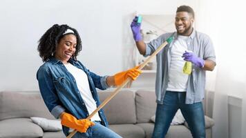 Spring-Cleaning With Fun. Joyful African American Couple Fooling Together While Tidying Their Apartment, Selective Focus On Woman photo