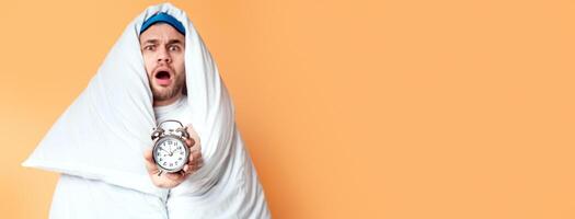 Man overslept concept. Emotional guy in blanket holding an alarm clock photo