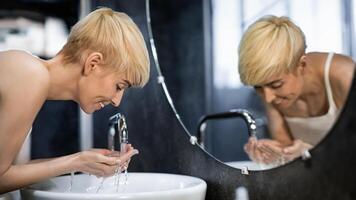 Cheerful Middle-Aged Lady Washing Face Standing In Bathroom. Hygiene And Skincare Routine. Selective Focus photo