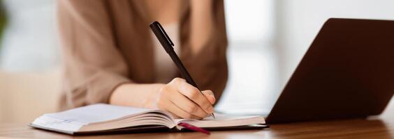 Taking Notes. Young secretary sitting at desk with laptop computer and talking on mobile phone, writing in notebook photo
