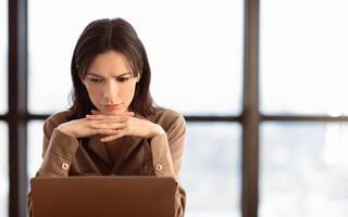 Problems At Work. Confused girl working on laptop, thinking about solution, empty space photo