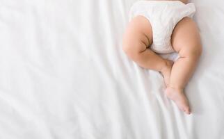 Baby legs and bottom in diaper on white bed background, top view, copy space photo