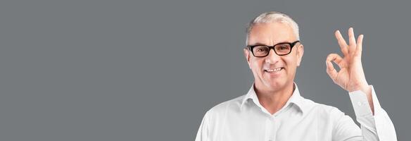 I'm Fine. Smiling senior man in specs showing ok gesture isolated over gray studio wall, copyspace photo