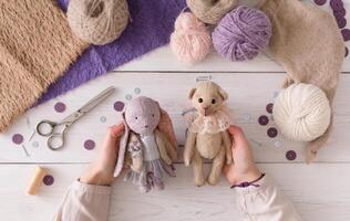 Process of making vintage toy, top view. Artisan pov, needlewoman hands holding handmade teddy bear and rabbit, home workshop photo