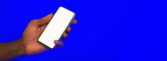 Male Hand Holding Cellphone With Empty Screen For Your Text Advertising Mobile Application On Blue Studio Background. Panorama, Mockup photo