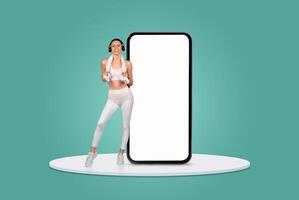 A woman in activewear is enjoying a dance workout while holding a game controller beside a large smartphone. She appears energetic and focused on her fitness routine. photo