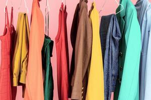 Shopping. Conceptual Shot Of Clothing Rail With Trendy Clothes Over Pink Background In Studio. Colorful Outfits Hanging On Hangers. Fashion And Style, Stylish Wardrobe Concept photo