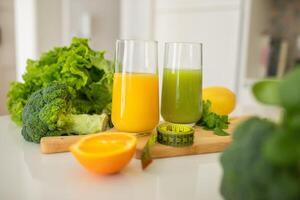 Two glasses filled with vibrant orange and green juices sit on a wooden board. Surrounding them are fresh broccoli, lettuce, and half an orange, enhancing the healthy atmosphere. photo