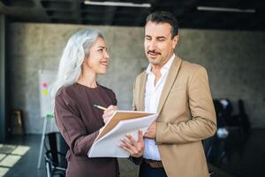 A woman and a man engage in a lively discussion in a contemporary office, with the woman taking notes on a notepad. Their expressions reflect collaboration and creativity. photo