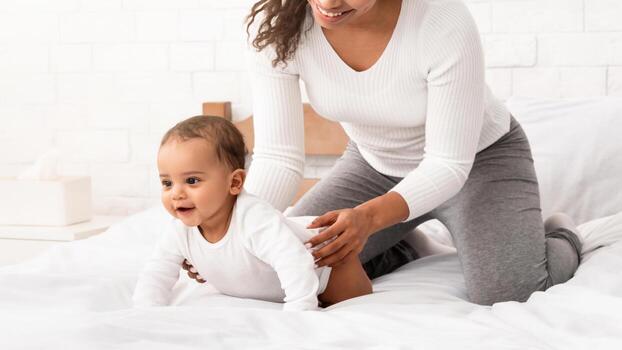 africano americano mamá jugando con infantil bebé Ayudar su pequeño hijo gatear en cama a hogar. mamá cuidando para toodler niño disfrutando maternidad rutina concepto foto