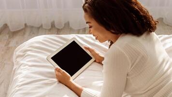 Over The Shoulder View Of Smiling Black Woman Using Digital Tablet With Empty Screen Enjoying Morning Reading E-Book Online Lying In Bed At Home On Weekend. Internet Website Advertising, Mock Up photo