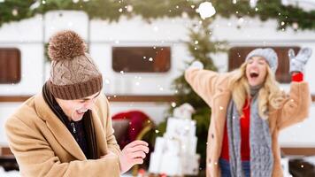 Two friends share laughter and joy while playing in the snow, surrounded by holiday decorations and a camper in a winter landscape. Their warm attire contrasts with the chilly weather. photo