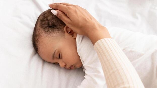 de la madre cuidado. negro de mamá mano acariciando dormido del bebe cabeza durante tiempo de día dormir en cama a hogar. recortado vertical disparo, parte superior vista. mamá cuidando para su infantil hijo mientras él duerme pacíficamente foto