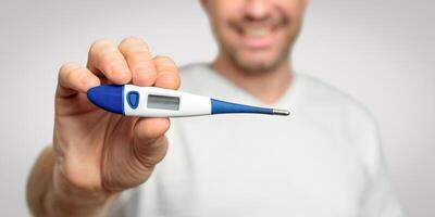 Illness Recovery. Healthy Man Showing Thermometer With Normal Temperature Smiling To Camera Over Gray Background. Panorama, Selective Focus photo